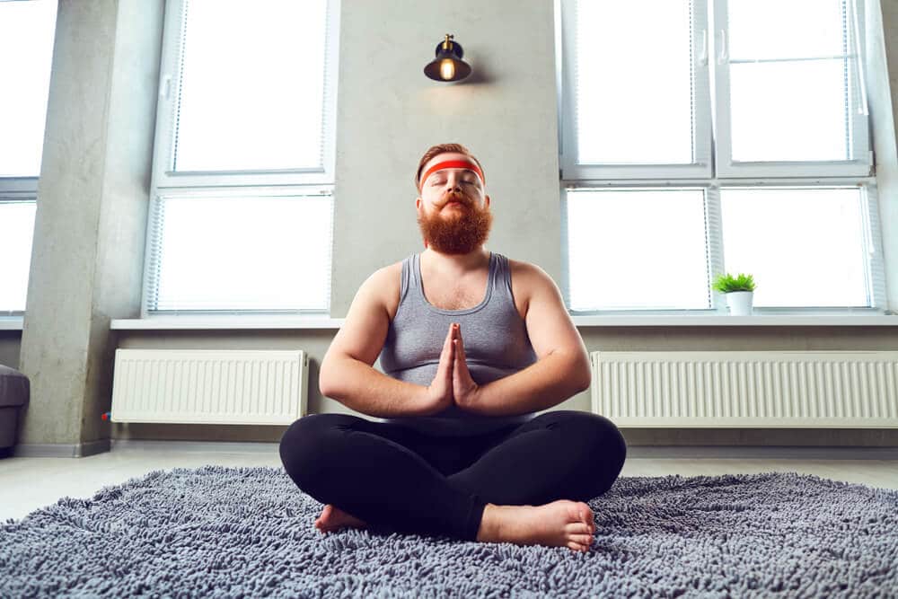 Homem meditando com pernas cruzadas e palma das mãos unidas.