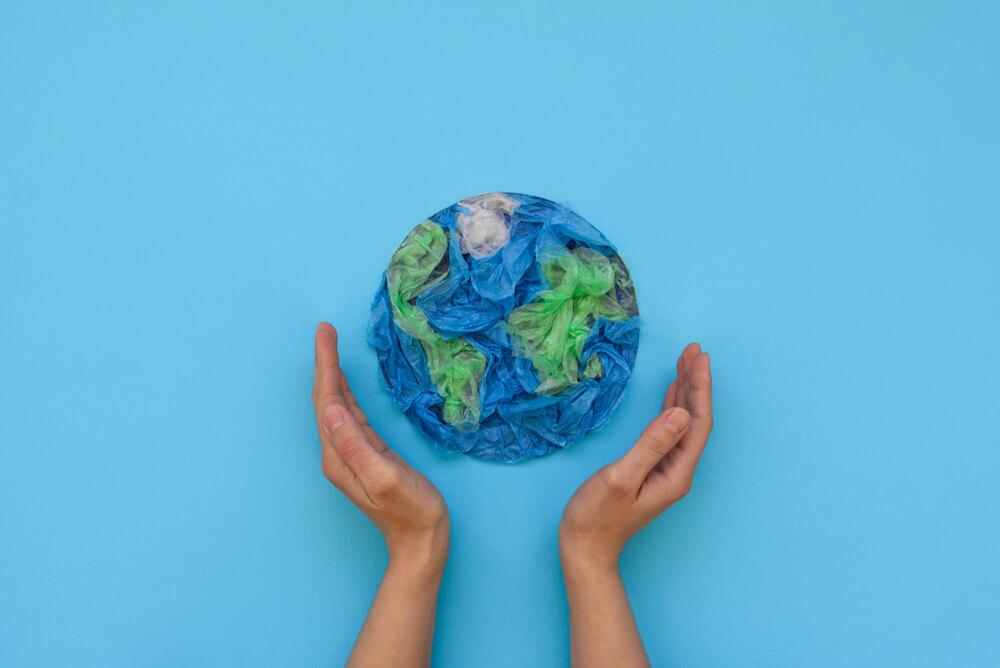 Pessoa com as mãos ao redor de um planeta Terra feito de papel crepom.