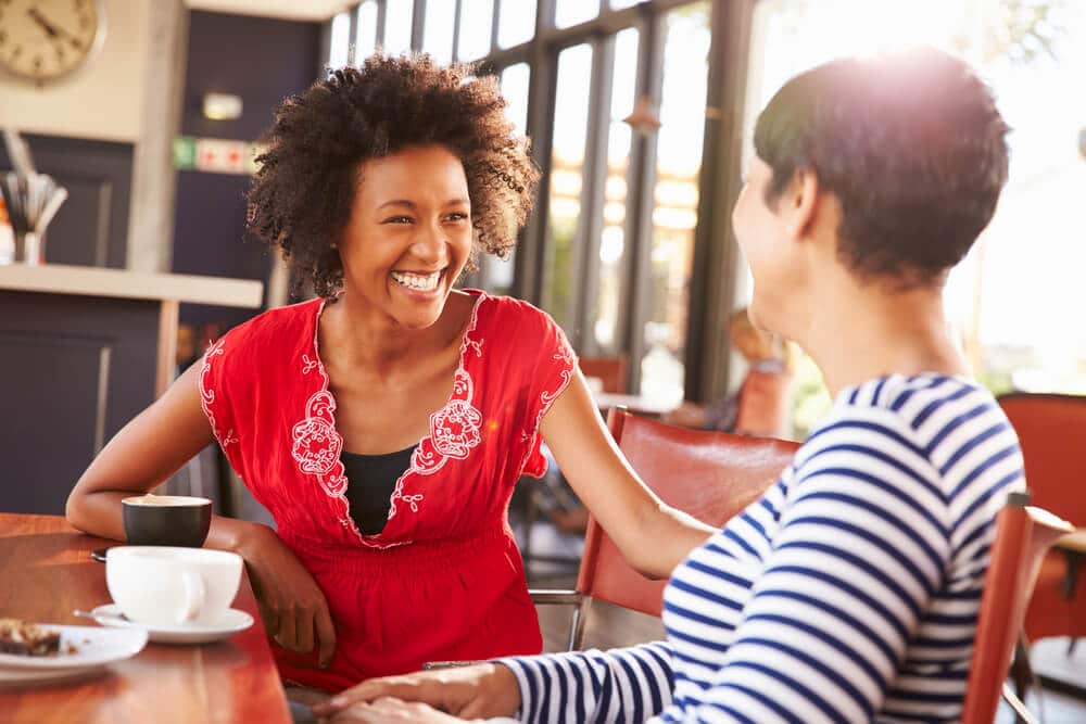Mulher negra sorrindo enquanto conversa com sua amiga.