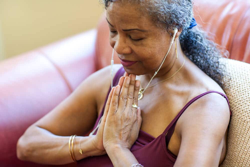 Mulher negra de meia idade meditando com as mãos próximas ao peito.